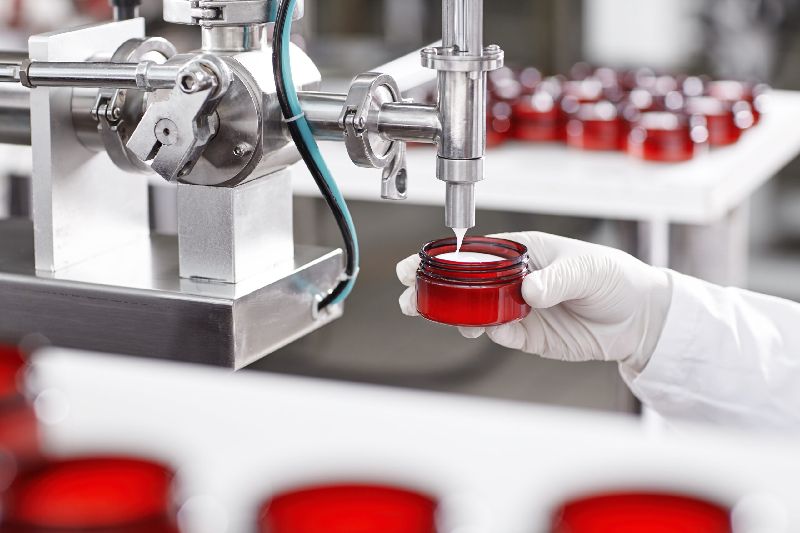 Portrait of big factory process of creating lotion for skincare. Researcher holding container under big metal tube pouring beauty cream isolated over working process at factory and many containers